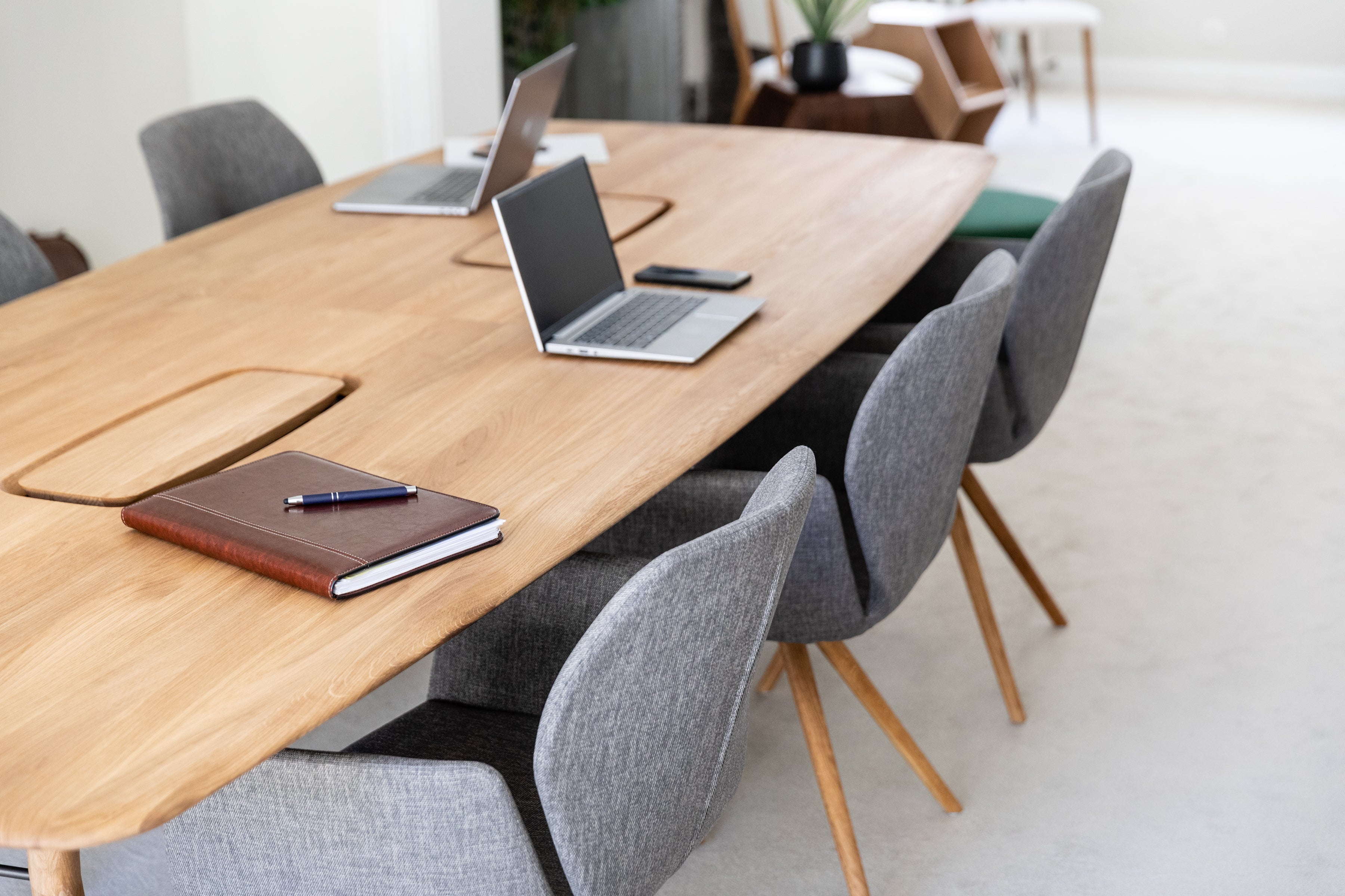 Long wooden table with gray chairs and laptops in a modern office setting