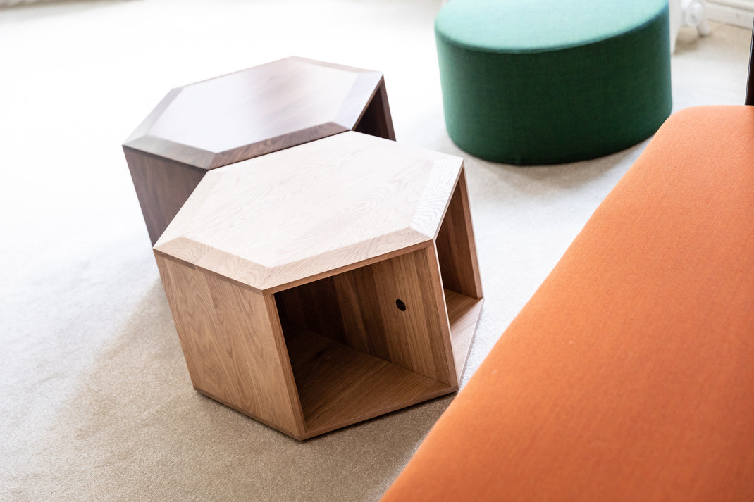 Hexagonal wooden side table with a green cylindrical stool and orange chair on a light-colored floor.