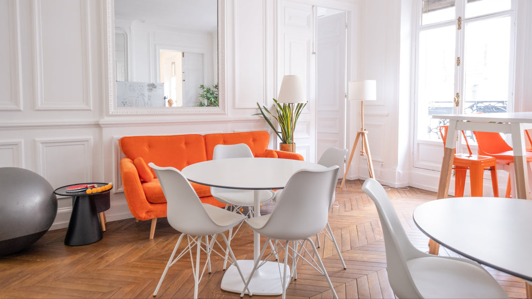 Modern living room with orange sofa, white chairs, and a round table.