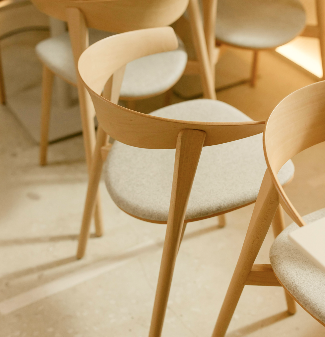 Wooden chairs with beige cushions arranged in a circle on a wooden floor.