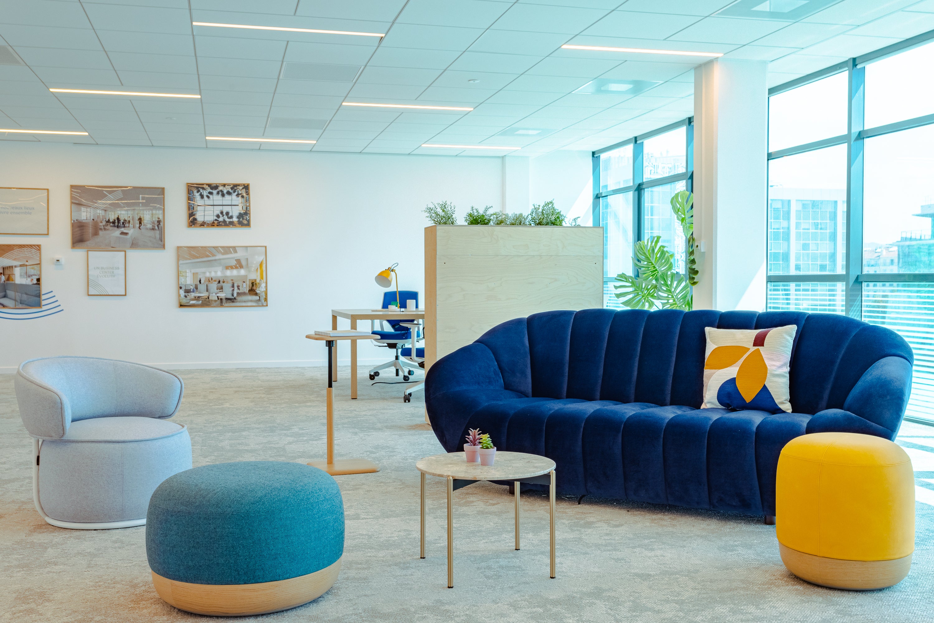 Modern office break out space with a blue sofa, yellow ottoman, and a desk.