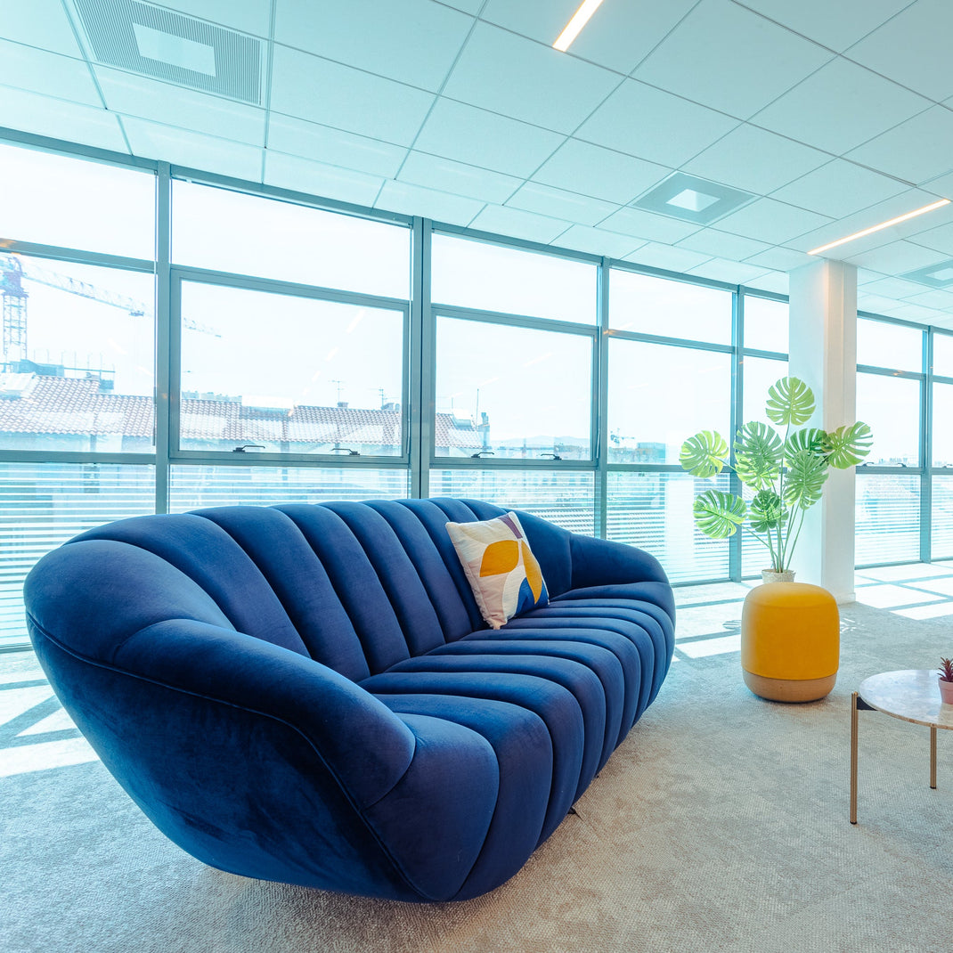 Modern office space with a blue sofa, round table, and large windows.