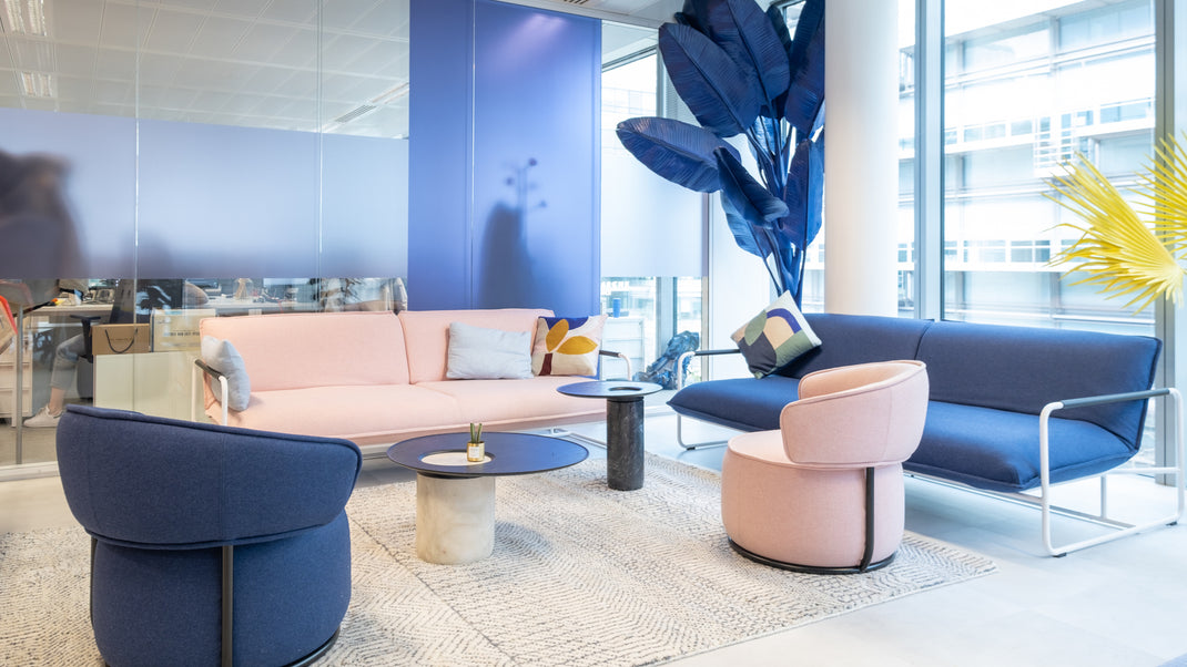 Modern living room with pink and blue furniture, including a sofa and chairs, in a bright office setting.