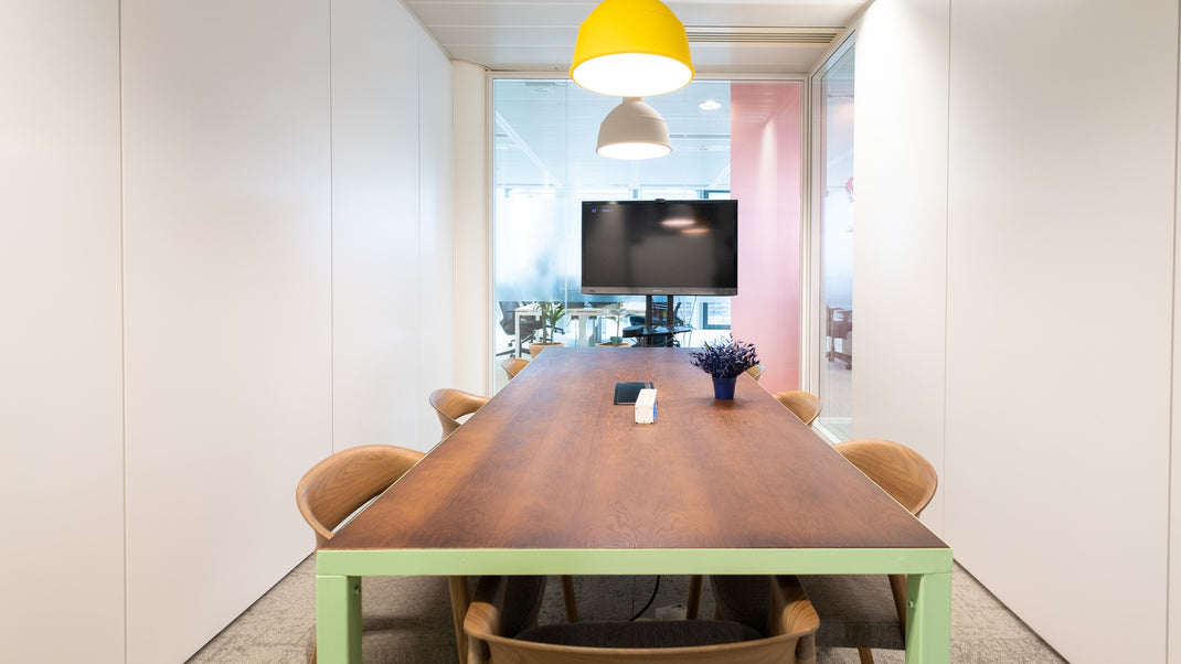 Modern conference room with a long wooden table and chairs, featuring a TV on the wall.
