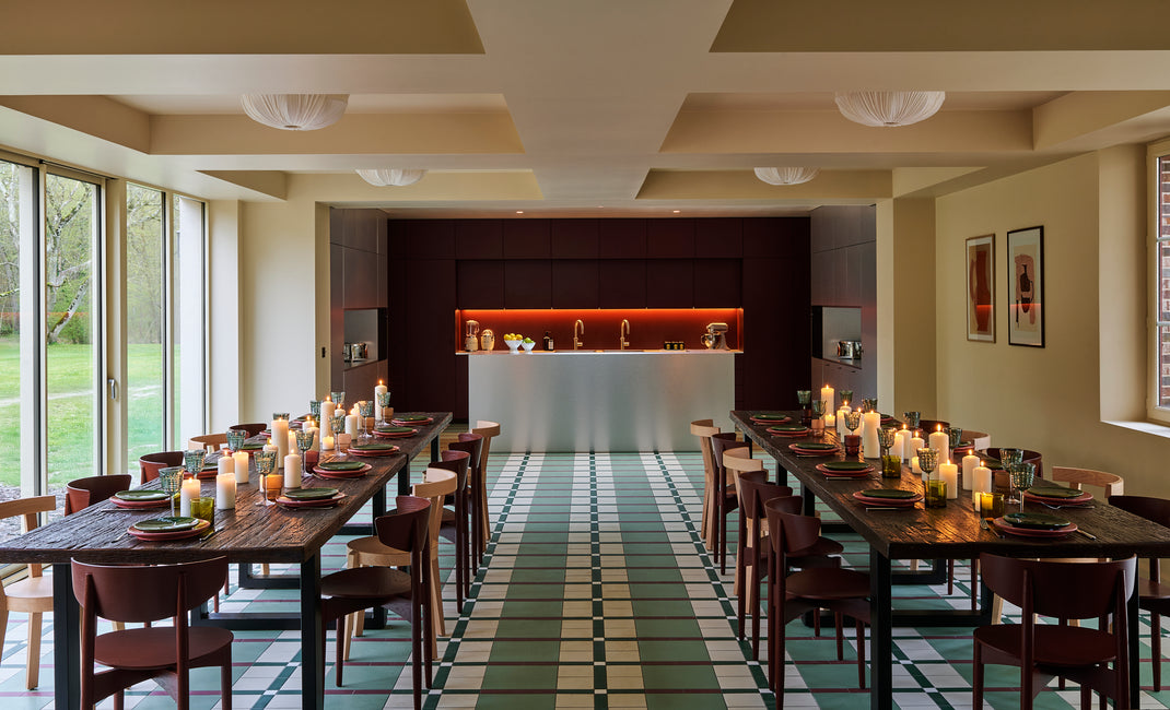 Modern dining area with long wooden tables, chairs, and a kitchen in the background.