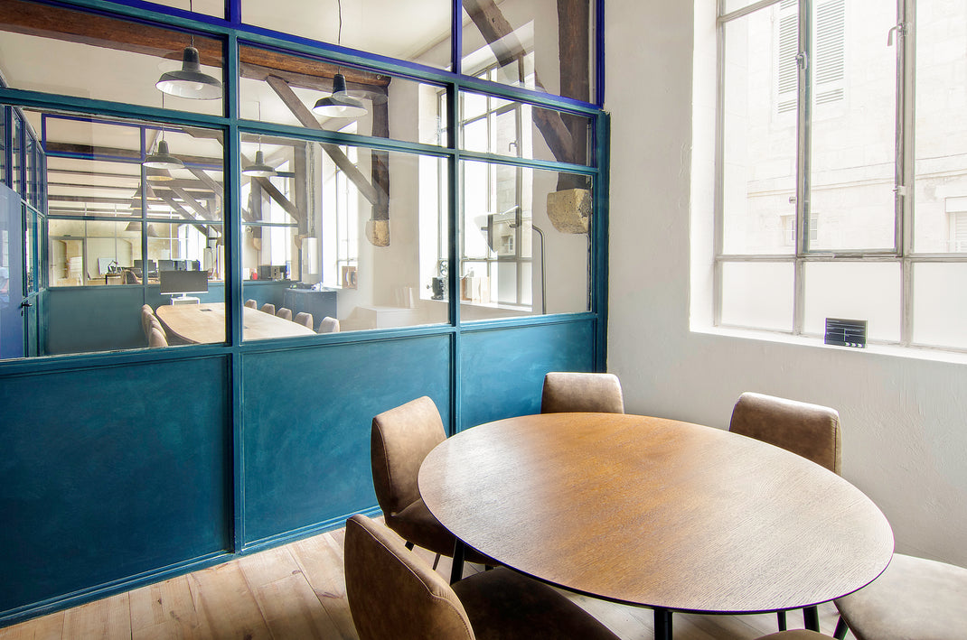 Modern office with round table and chairs near a glass wall.