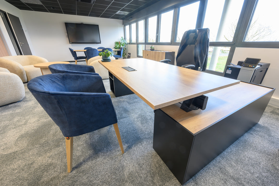 Modern office space with a large desk, chairs, and a TV in the background.