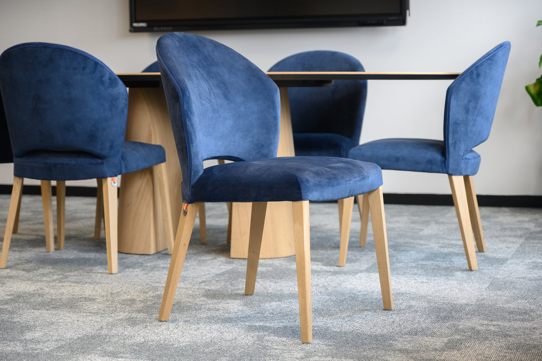 Blue velvet chairs with wooden legs arranged around a table in a room.