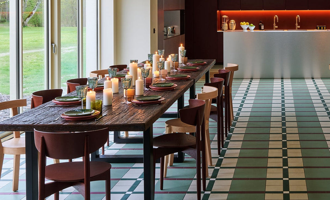 Modern dining area with long wooden tables, chairs, and a kitchen in the background.