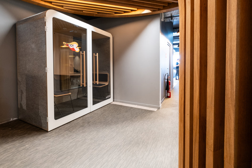 Modern office pod with glass doors in a neutral-colored room.