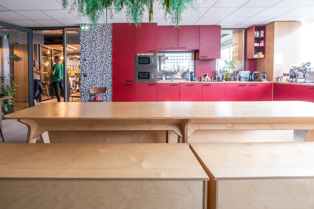 Modern kitchen in office with red cabinets, wooden tables, and people in the background