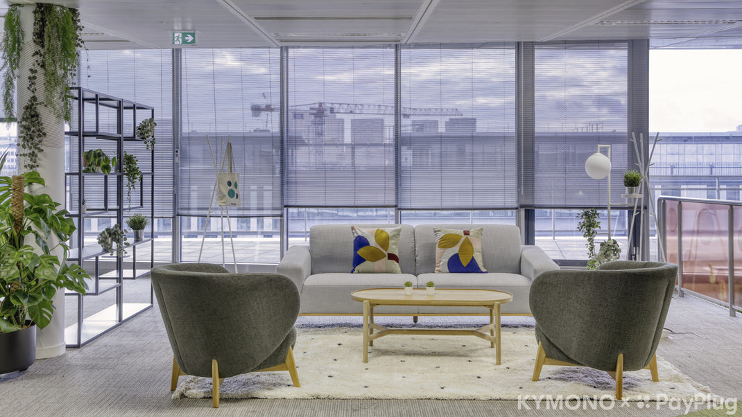Modern office lounge with a sofa, chairs, and coffee table near large windows with a cityscape view.