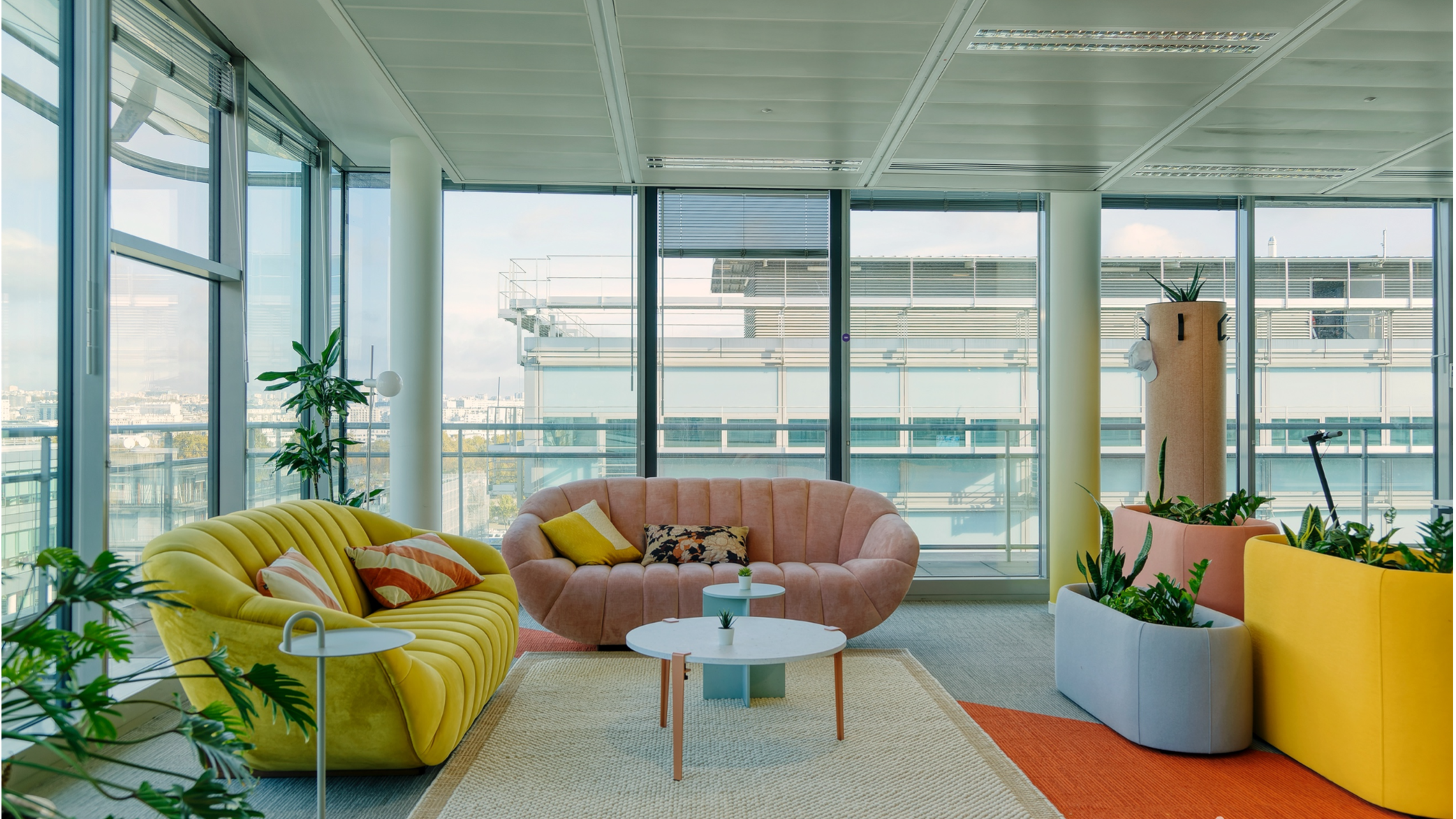 Office lounge area with yellow and peach colour couches, tiptoe coffee table, modern metal side tables and coloured planters.