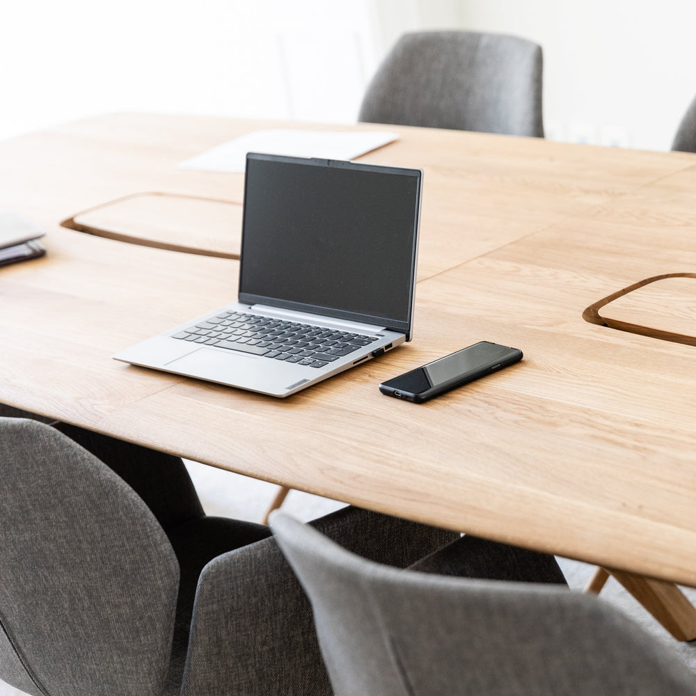Wooden office table with laptops, phone, and headphones in a meeting room.