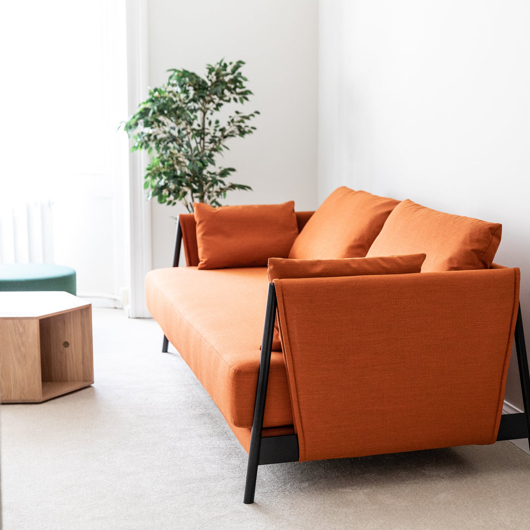 Orange sofa with black legs in a room with white walls and a plant.