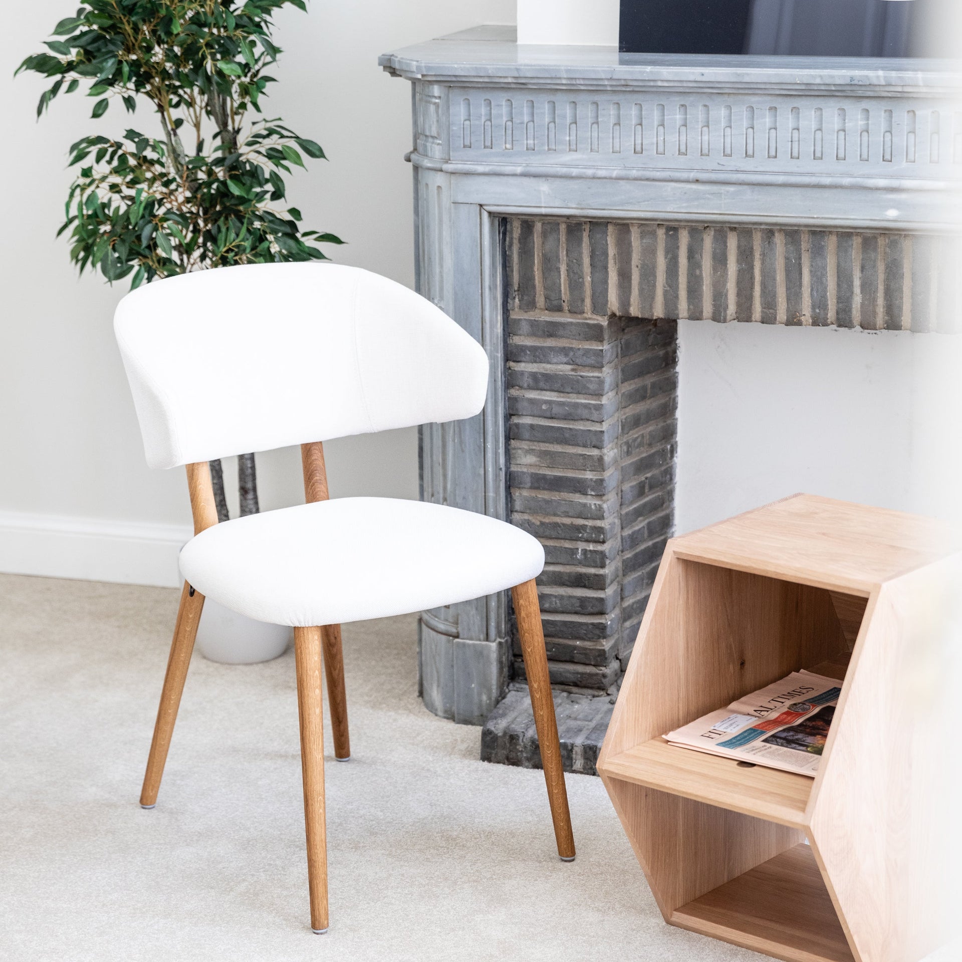 White chair with wooden legs in a room with a fireplace and plant