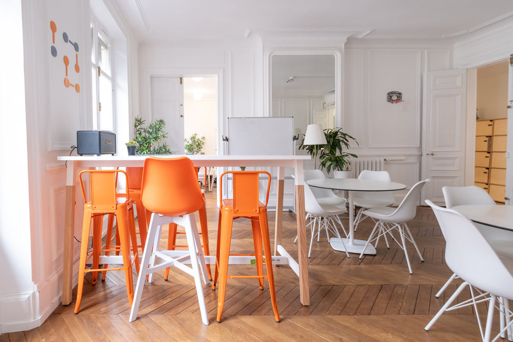 Modern kitchen with orange stools and white chairs around a dining table.