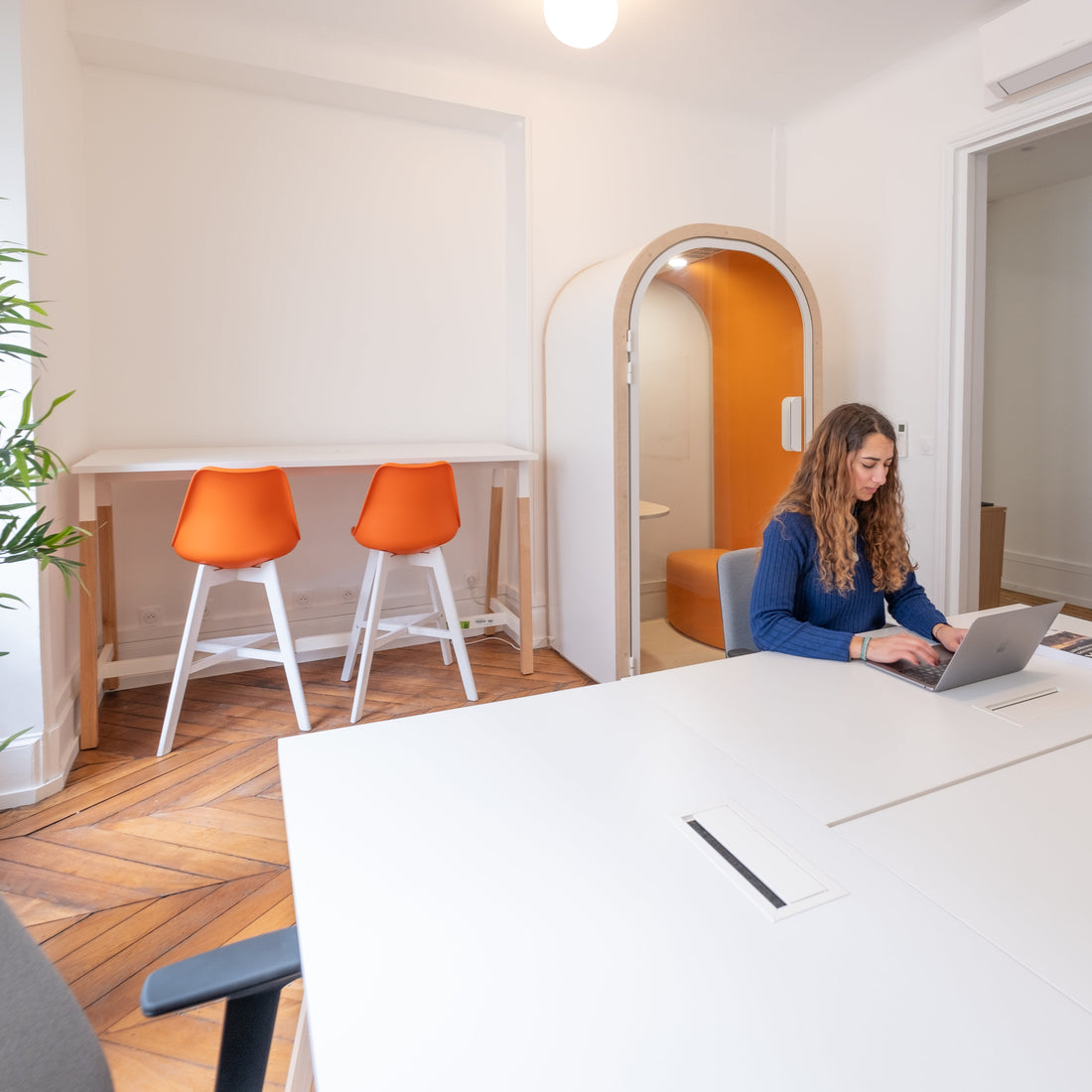 Open office space with white desks, and orange accented furniture and phonebooth. 