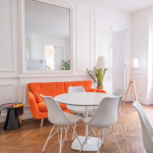 Modern break out area in an office with orange sofa, white chairs, and a round table.
