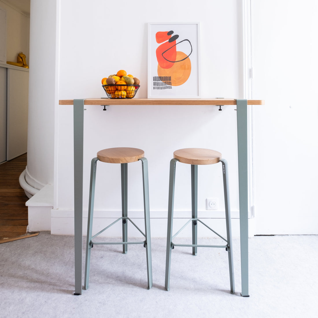 High table with stools and a colorful abstract painting on a white wall.