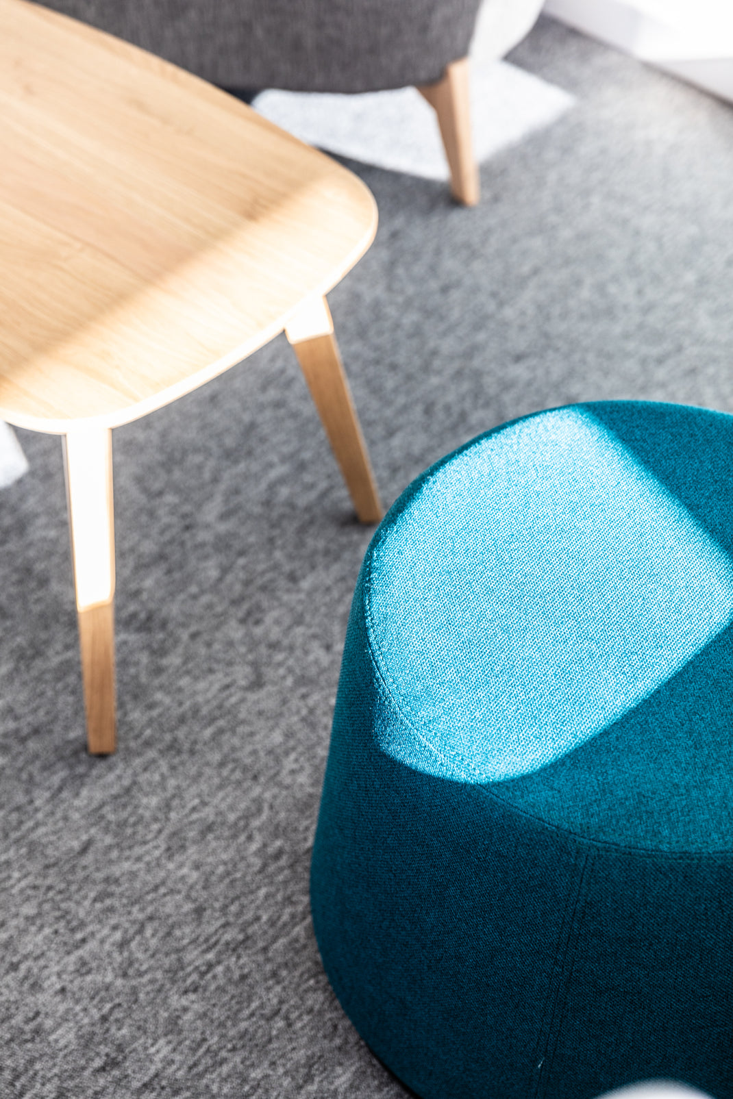 Teal and blue footstool on a gray carpet with a wooden stool in the background.