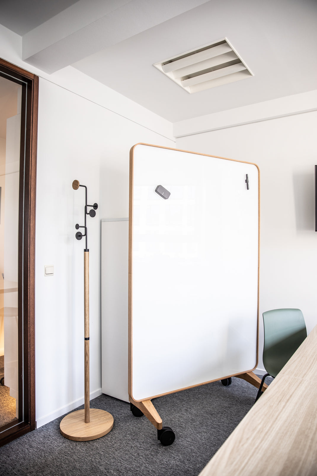 Room with a standing whiteboard on wheels, coat hangar, and chair.