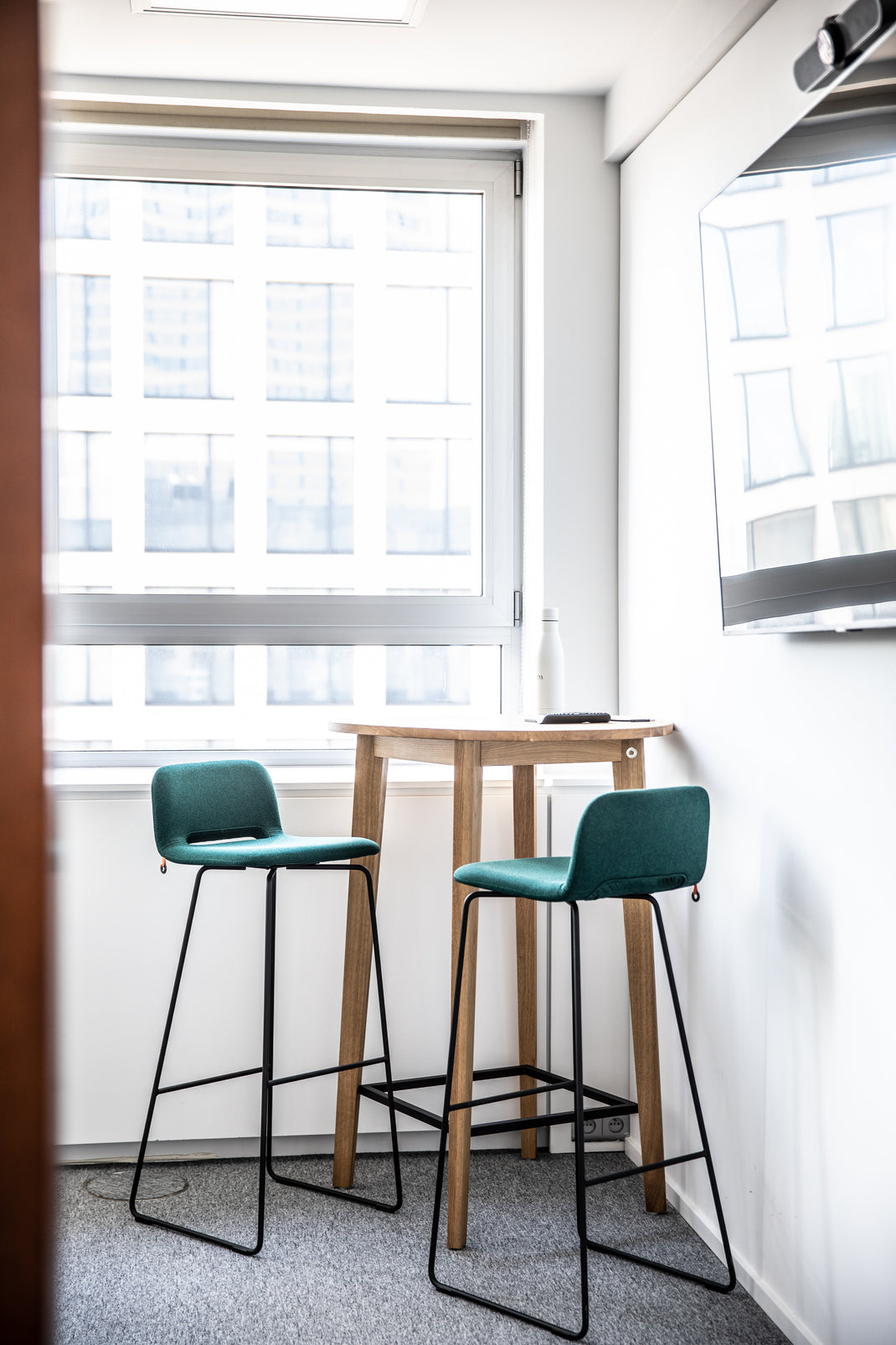 Two green bar stools in front of a small wooden table near a window.