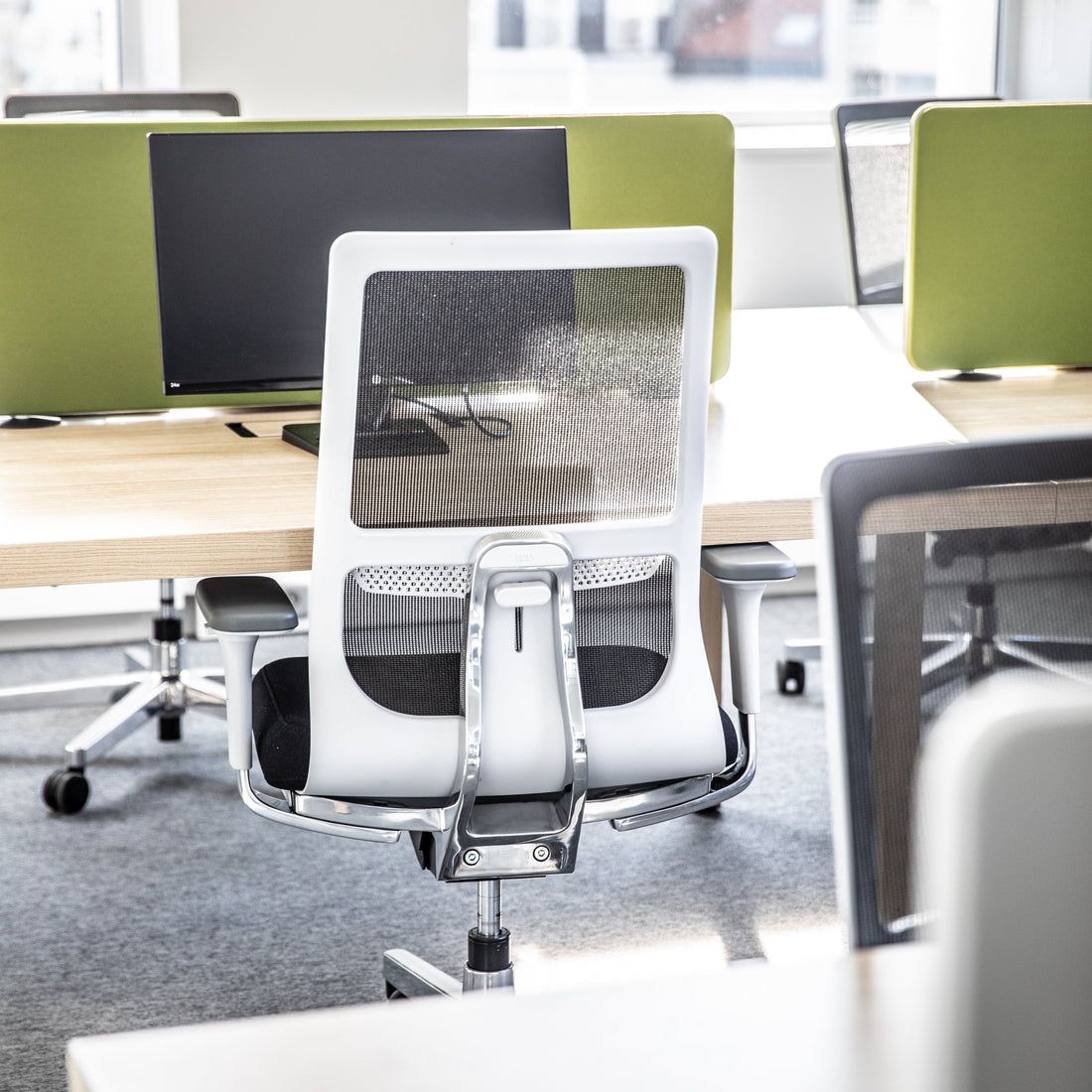 Modern ergonomic office chair in a bright office setting with desks and computer monitors.