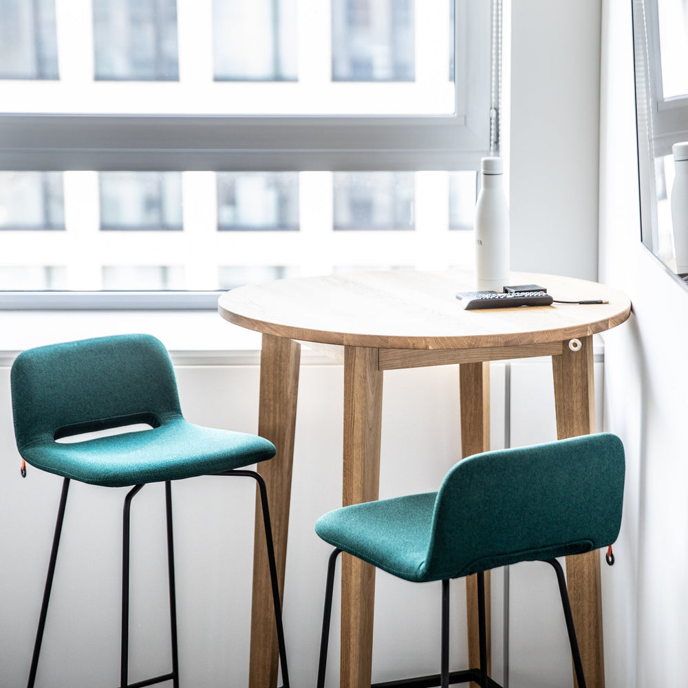 Two teal bar stools in front of a wooden table near a window.