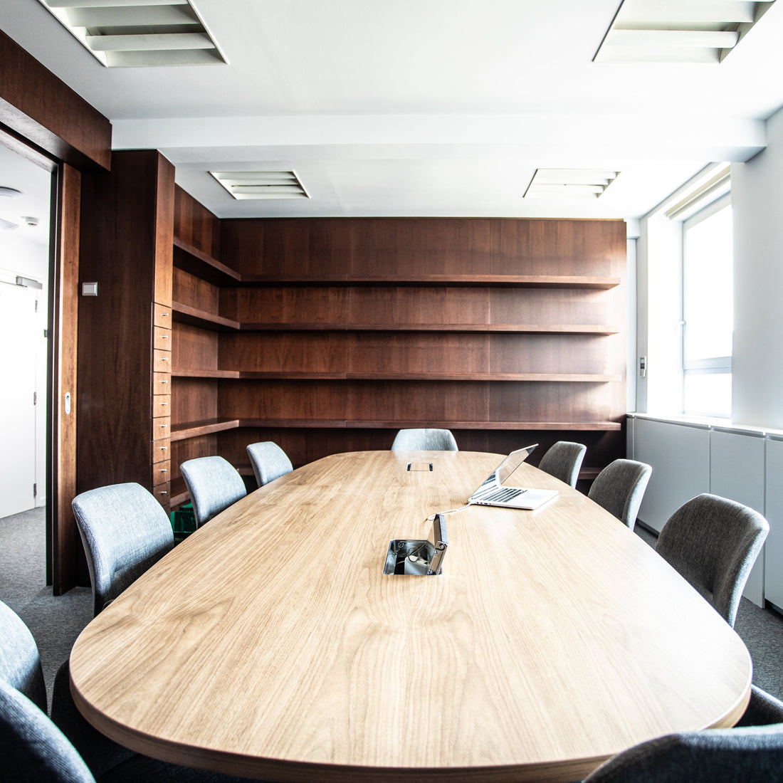 Modern conference room with a long wooden table and chairs. Floor to ceiling bookcase. 