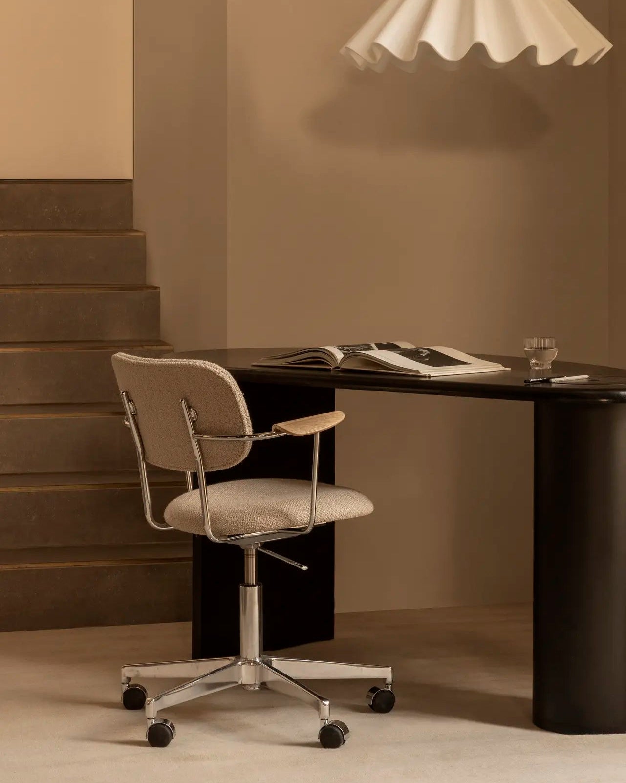 Modern office setup with a desk, chair, and pendant light in a neutral setting.