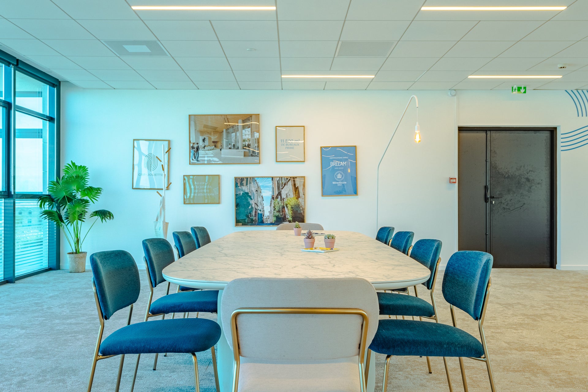 Modern conference room with a large marble top table and blue fabric office chairs, featuring artwork on the wall.