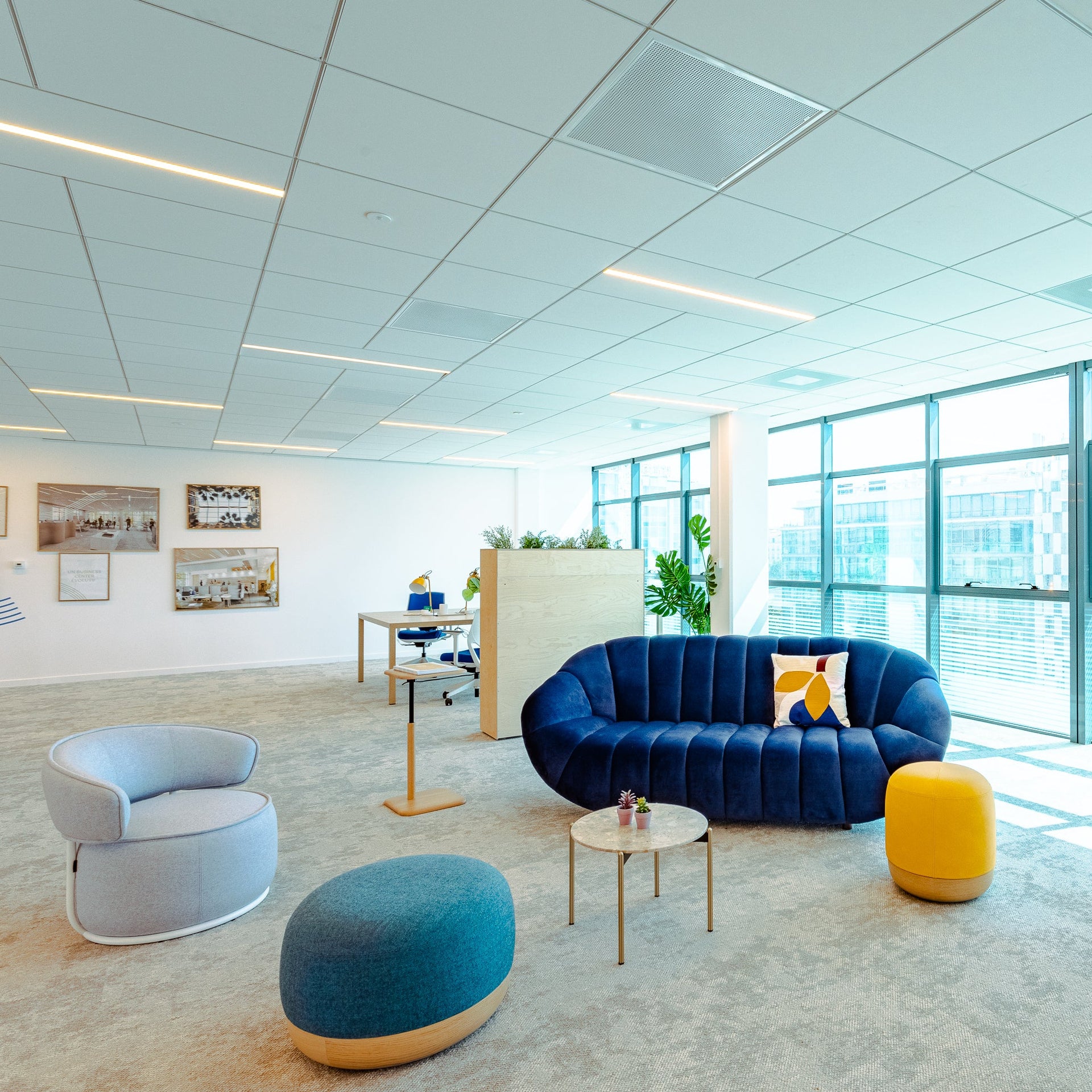 Modern office space with blue sofa, armchair, and ottoman near large windows.