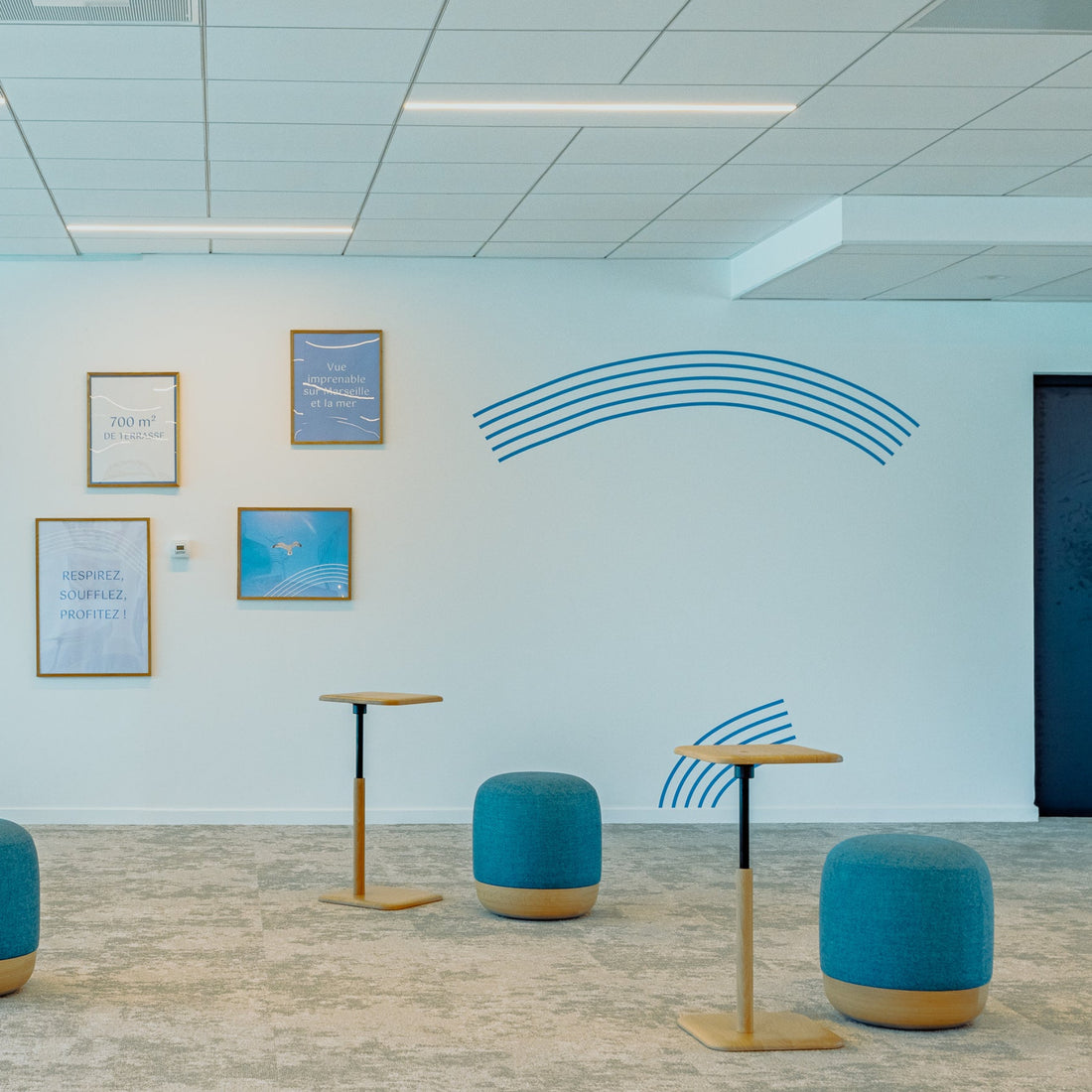 Modern office space with blue stools and tables on a light gray floor.