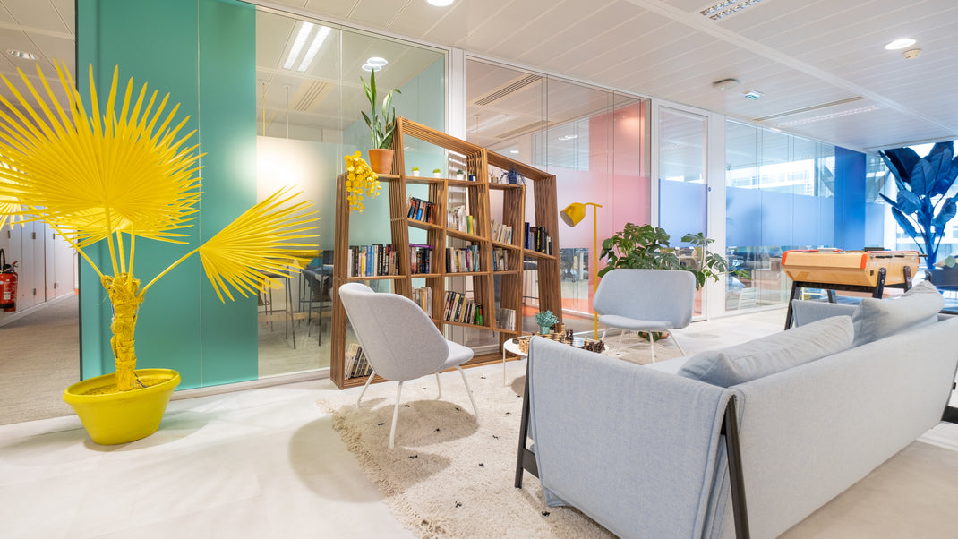 Modern office interior with a yellow plant, bookshelf, and seating area.