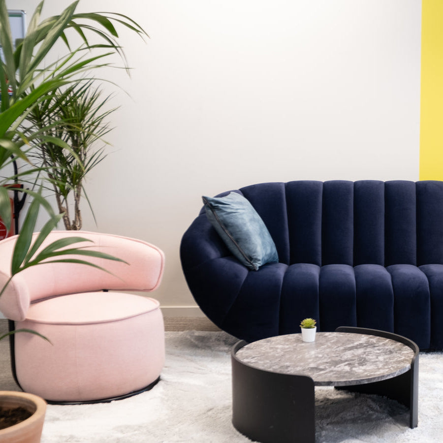 Modern living room with a navy blue sofa, pink armchair, and yellow wall.