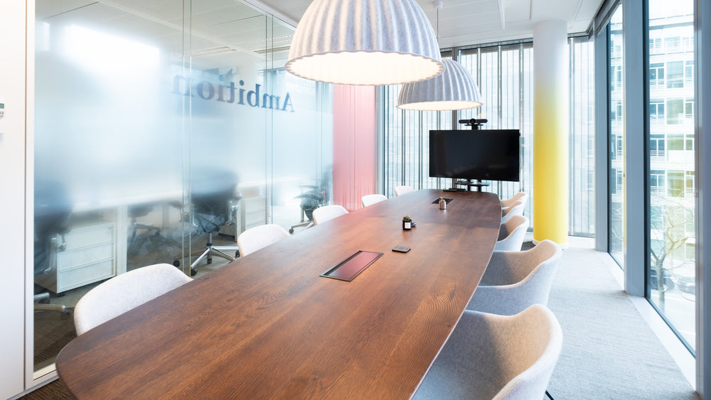 Modern conference room with a long wooden table and white chairs, featuring a large window and office branding.