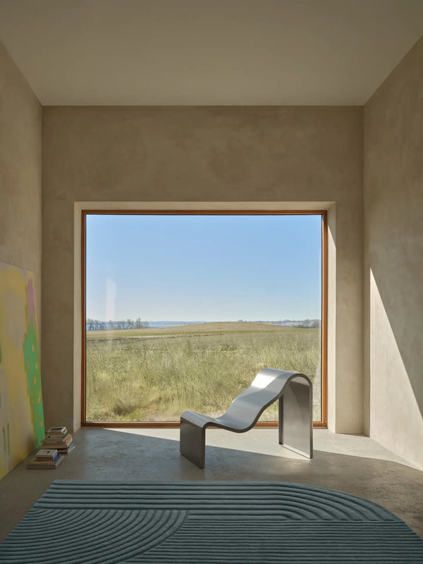 Modern room with a large window view of a field and sky, featuring a unique chair.