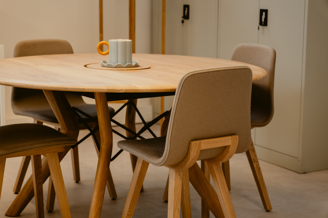 Round wooden dining table with four chairs in a minimalistic room.