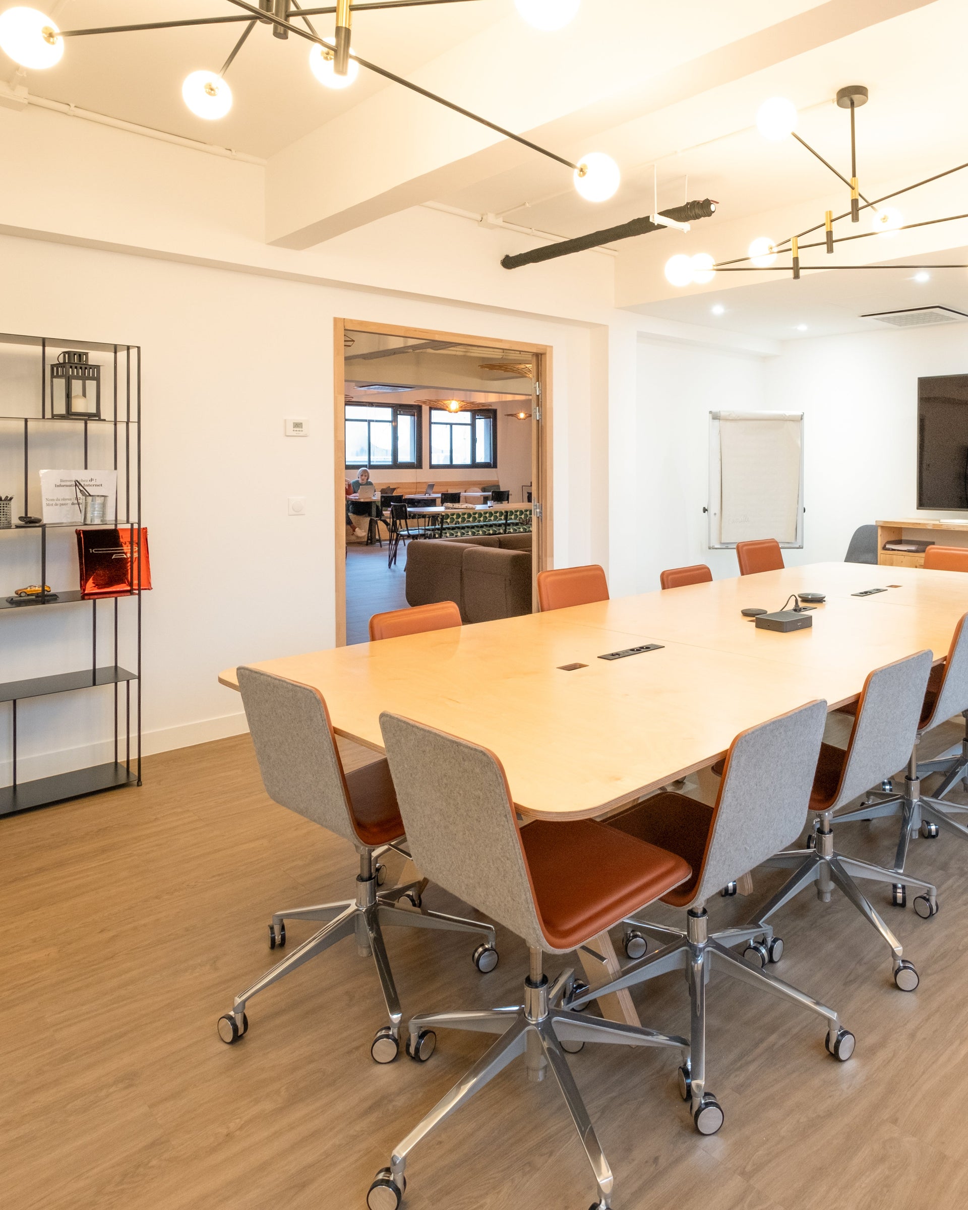 Modern conference room with a long wooden table and chairs, a TV, and office decor.