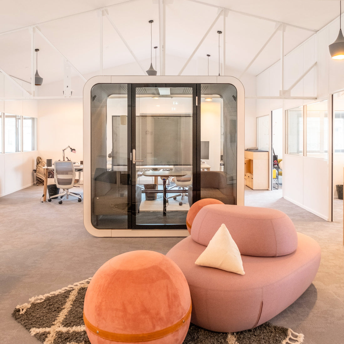 Modern office space with pink and orange furniture, glass partition, and wooden cabinets.