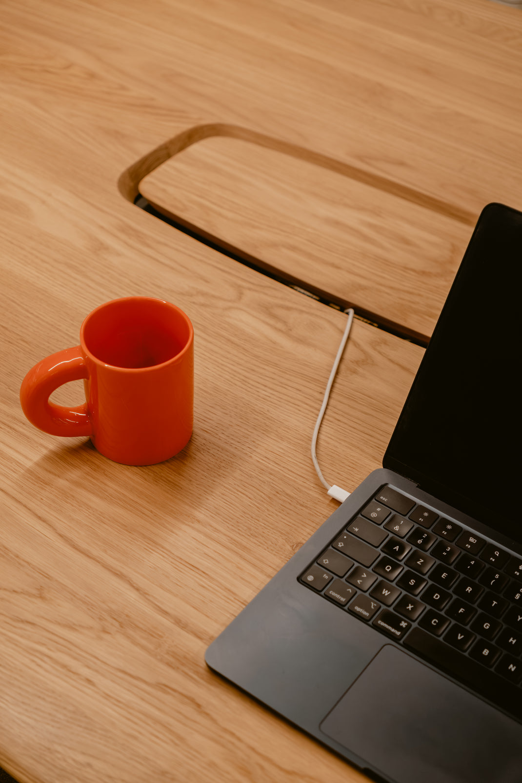 Orange mug and open laptop on a wooden table