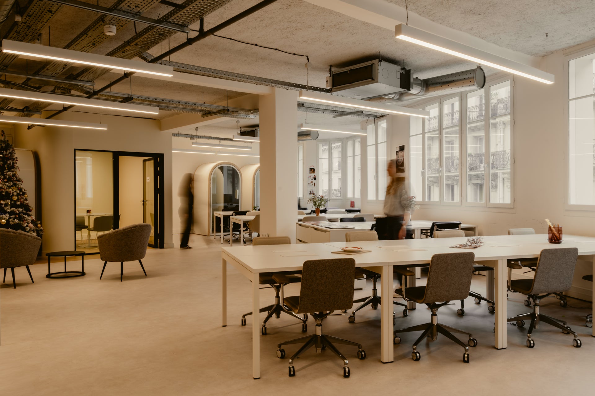 Modern office space with large windows, a long white table, and ergonomic chairs.