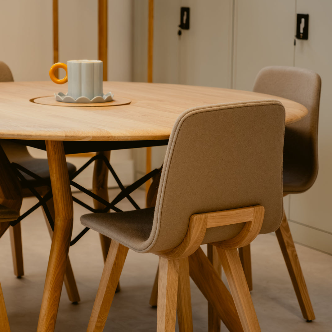 Round wooden dining table with four chairs in a minimalistic room.
