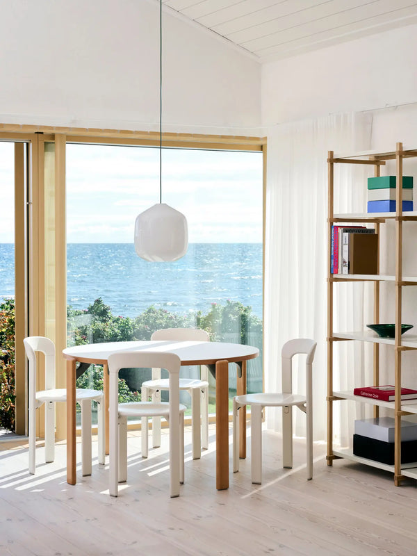 Modern interior with a dining table and chairs by a large window with a view of the ocean.