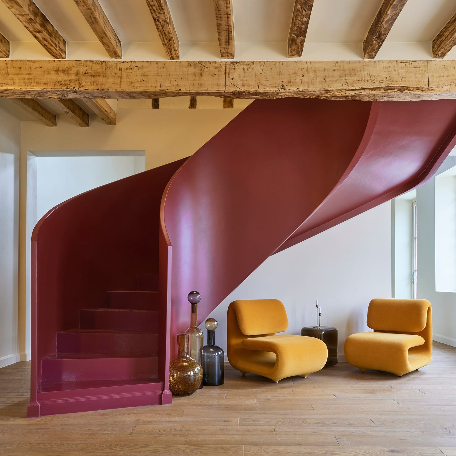 Modern interior with a red spiral concrete staircase and yellow plush chairs.