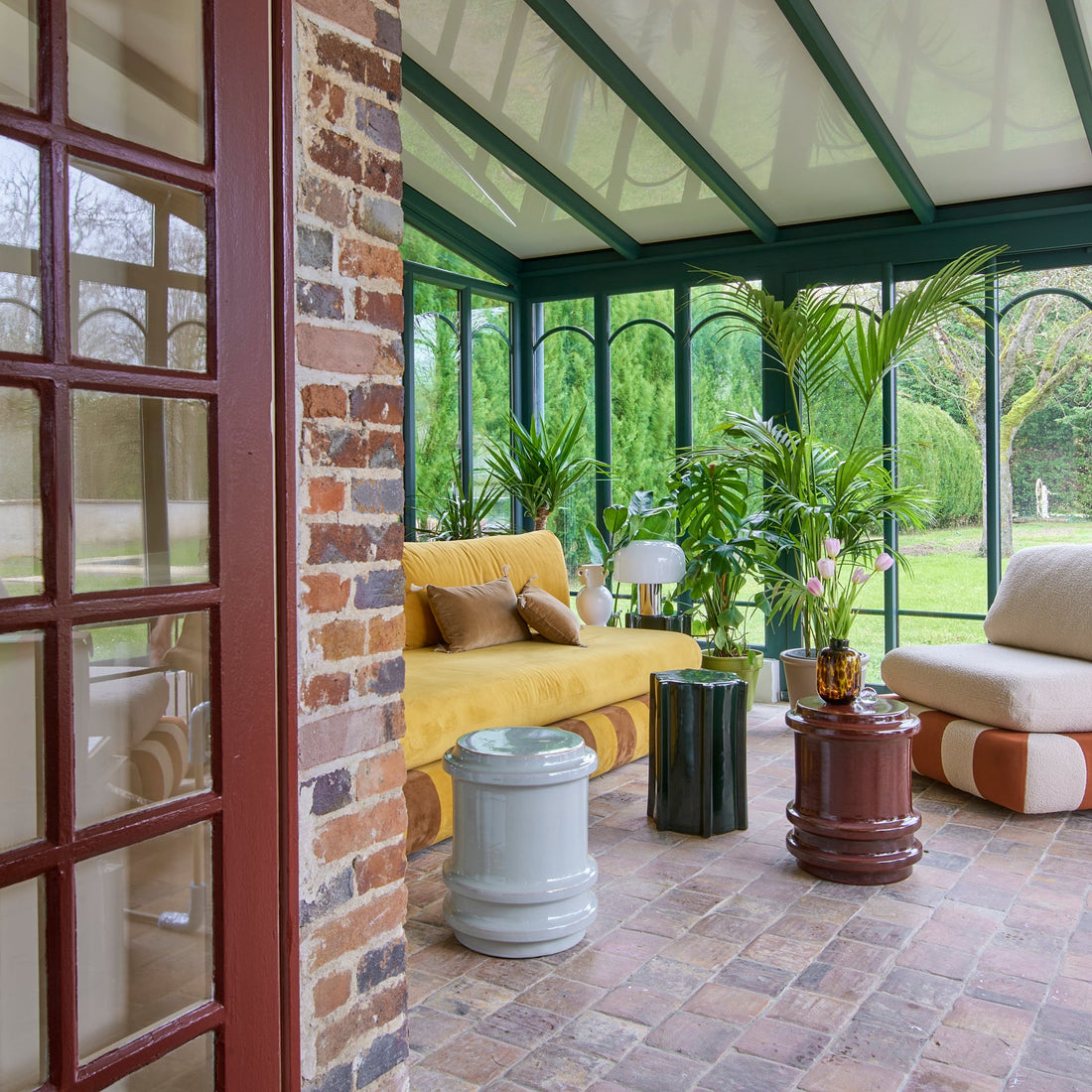 Sunroom with yellow sofa, plants, and large windows overlooking a garden.