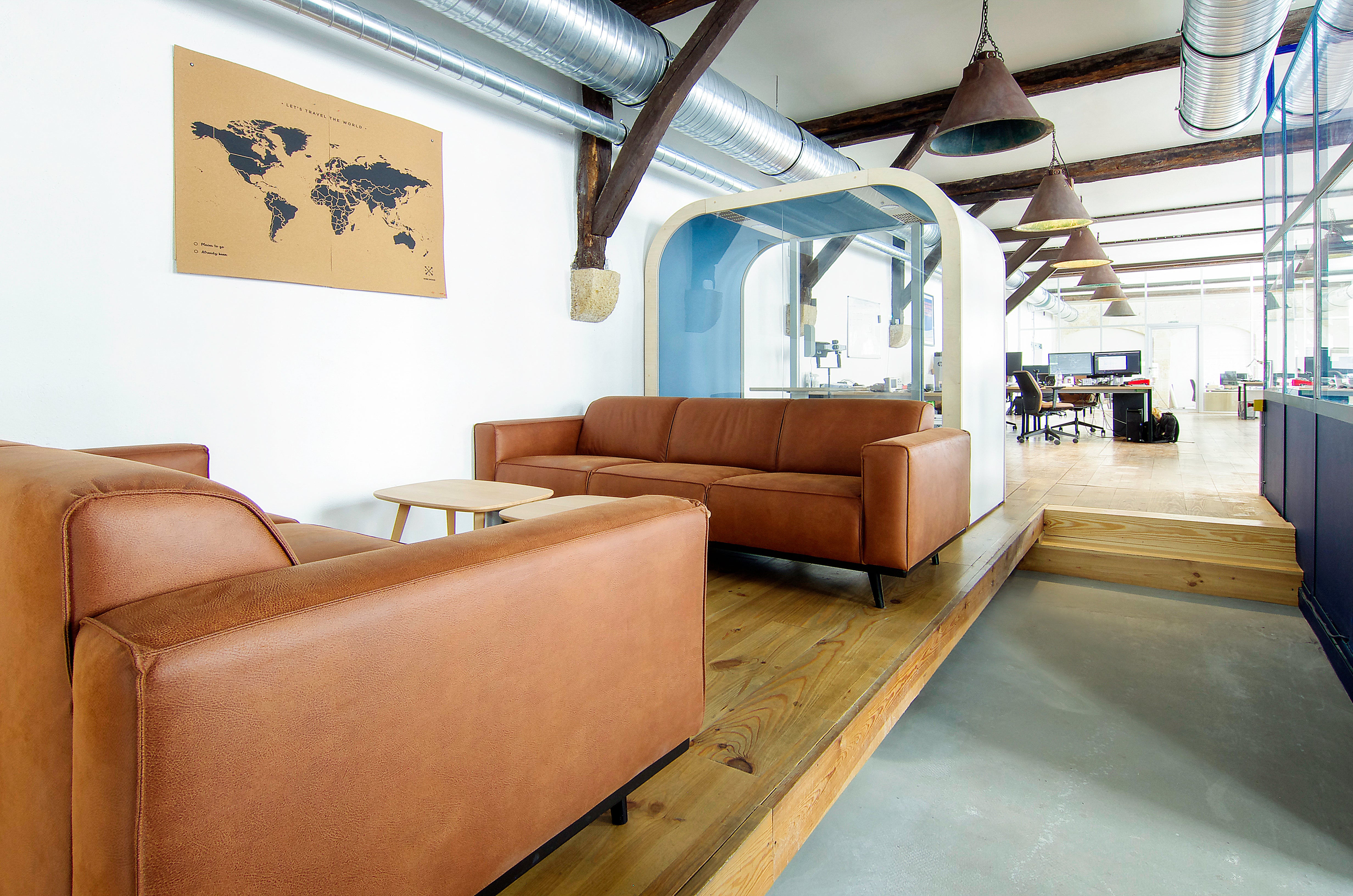 Modern office space with brown leather couches, a world map on the wall, and a glass wall.
