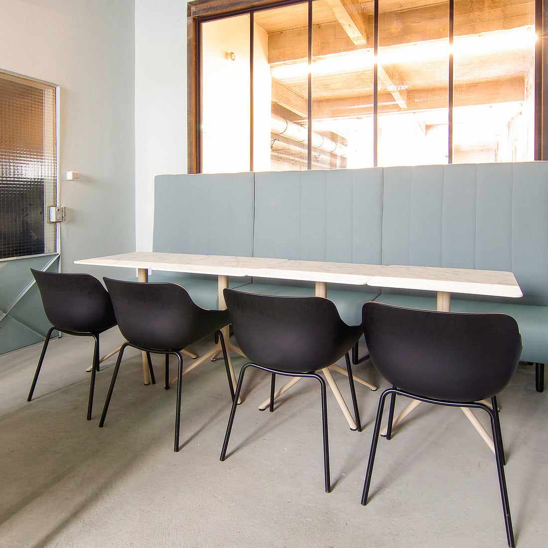 Modern office break room with gray booth seating and black chairs.