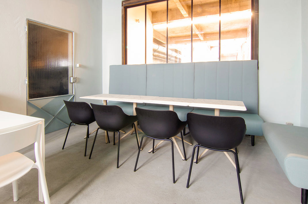 Modern office break room with gray booth seating and black chairs.